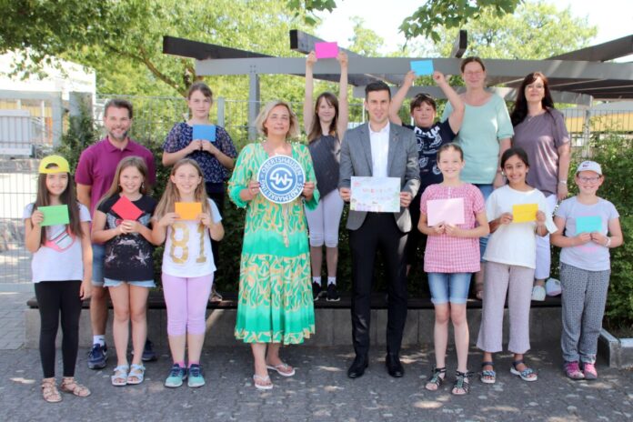 22_28_PT_OBH_Adventskalender-Gewinner_Bild_3 Grundschüler stehen mit Erwachsenen vor einer Bank und halten Briefe und Bilder in den Händen.